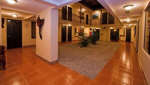 A spacious indoor area with a tiled floor, a central plant, and a staircase leading to an upper level. - Hotel El Cerro (Liberia)