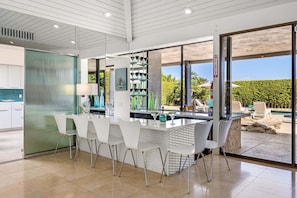 A modern kitchen with a bar area, white chairs, and a view of the outdoor pool.