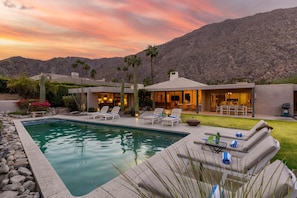 A pool with lounge chairs, a patio area, and a mountain backdrop.