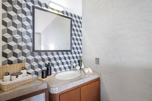 Une salle de bain avec un mur orné d’un motif géométrique, un grand miroir, un lavabo et un meuble en bois.