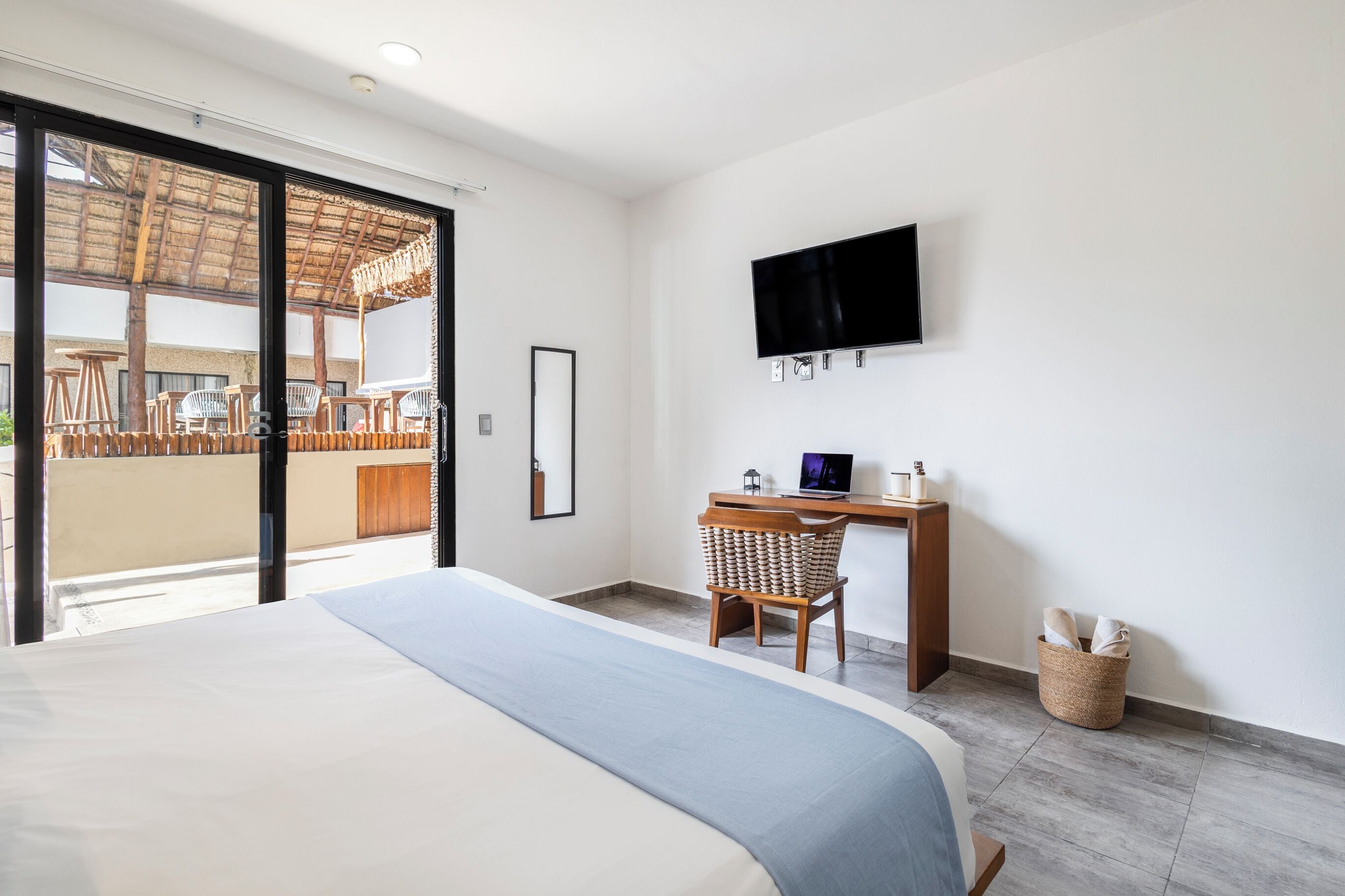 Una habitación de hotel moderna con una cama grande, un escritorio con una computadora portátil, un televisor y un balcón con mobiliario exterior.