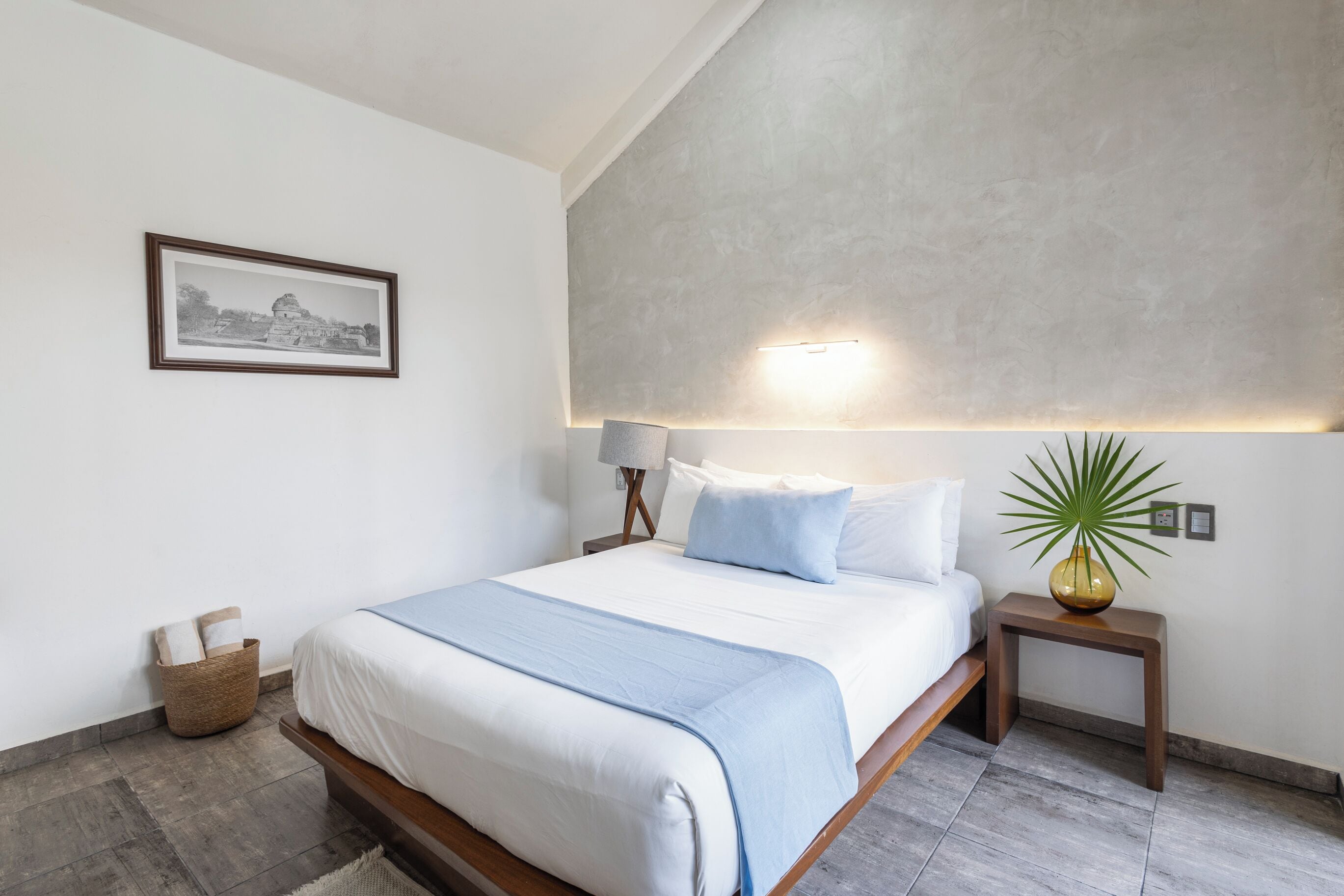 A modern bedroom with a bed, bedside tables, a lamp, a framed picture, and a potted plant.