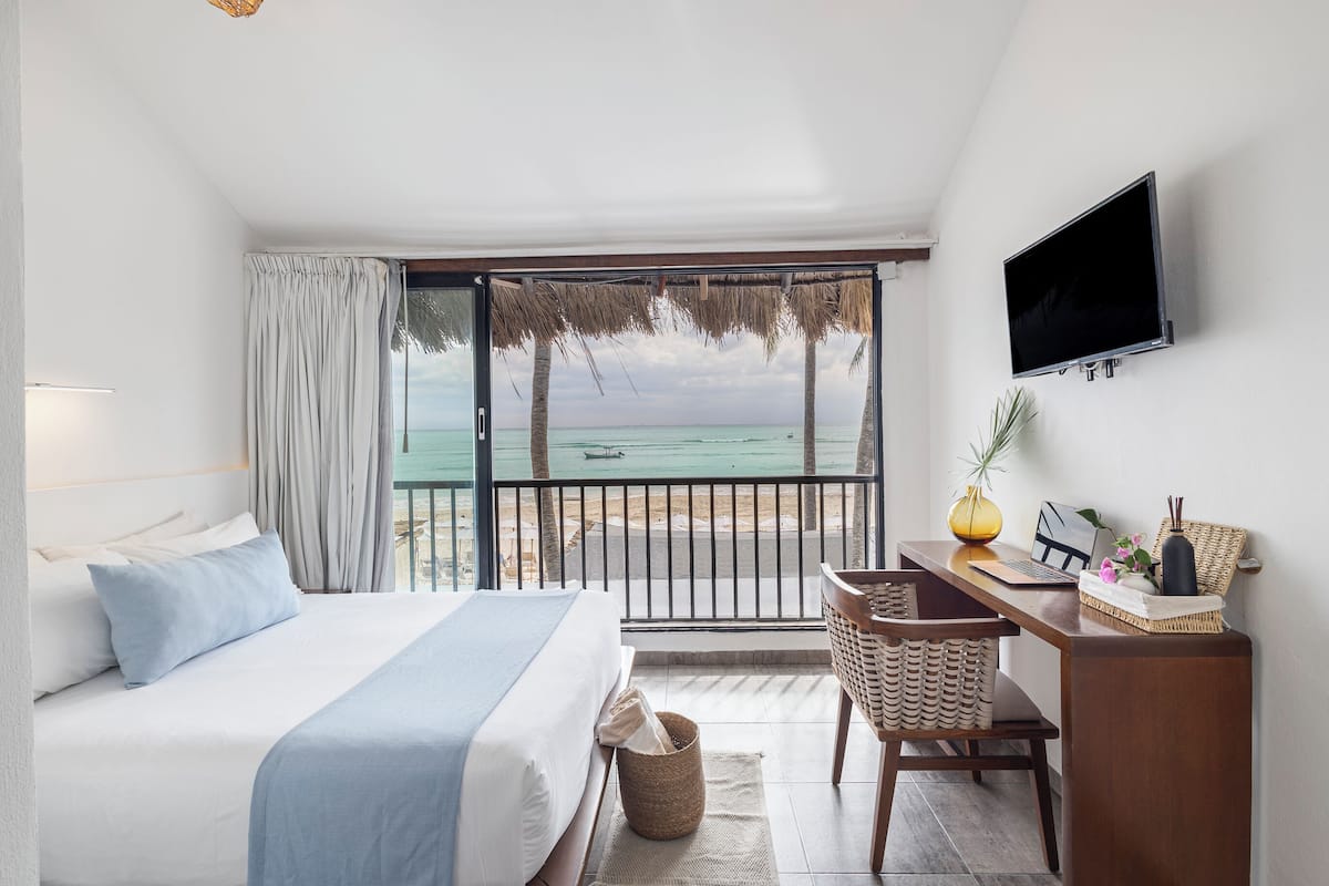 Ein Schlafzimmer mit Bett, Schreibtisch, Stuhl, Fernseher und Blick auf den Strand.