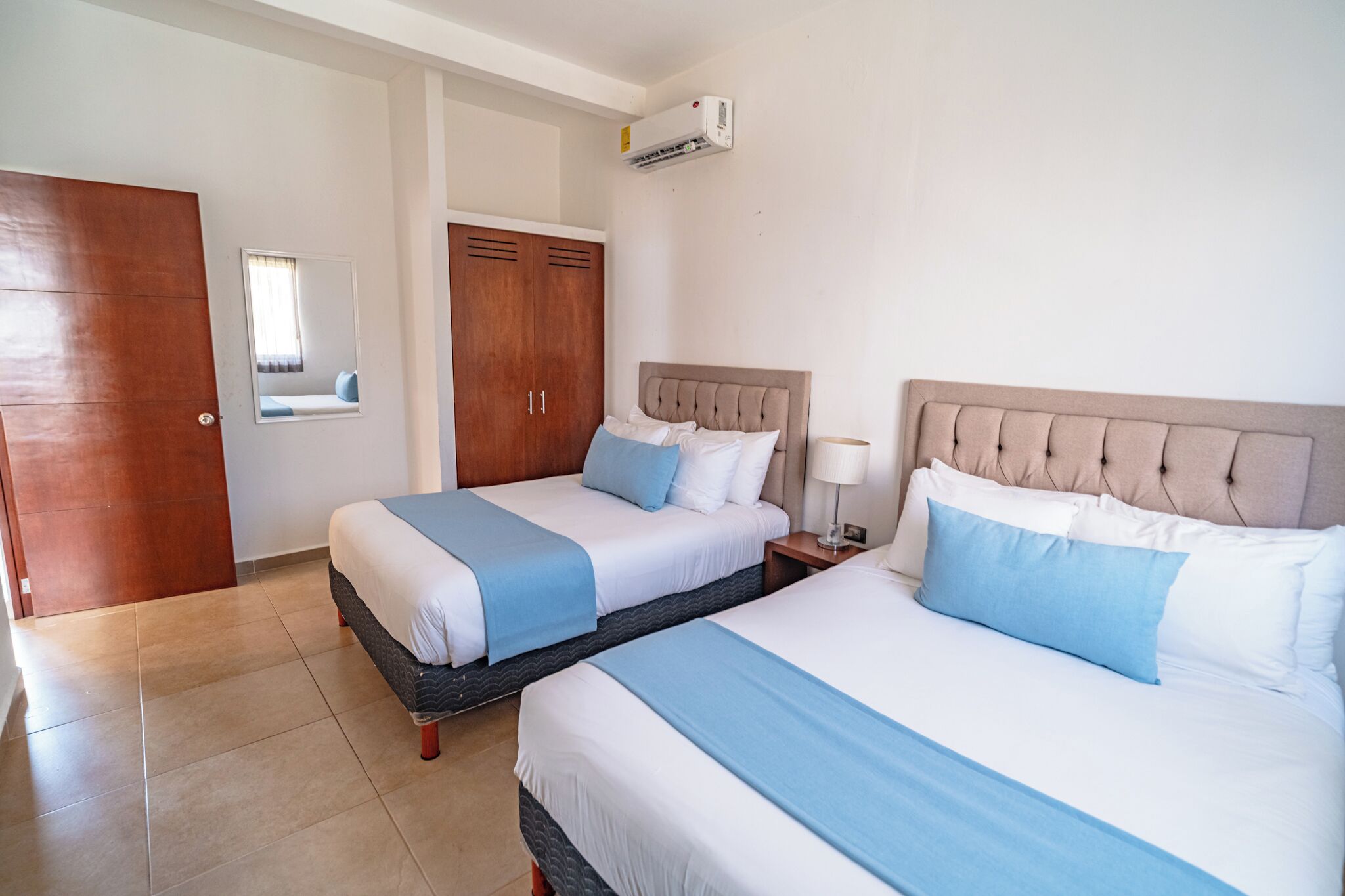 Een hotelkamer met twee bedden, een kledingkast, een spiegel en een airconditioning.