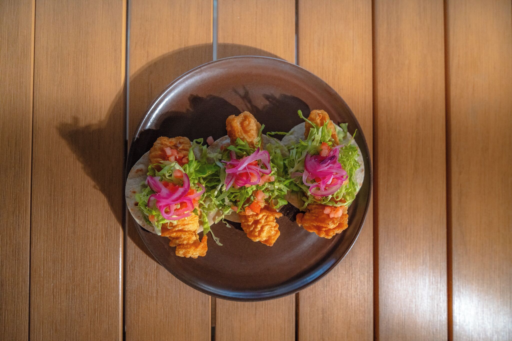 A plate of food with lettuce, tomatoes, and pink onions on a wooden table.