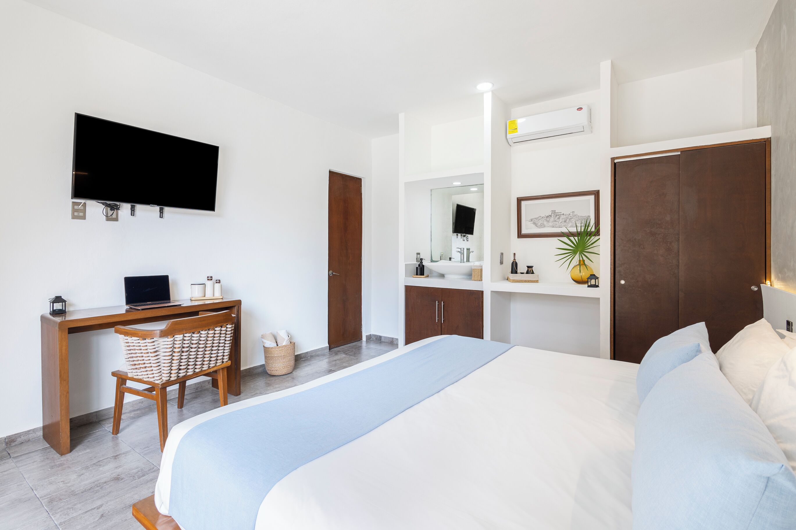 Ein modernes Hotelzimmer mit Bett, Schreibtisch mit Computer, Fernseher, Badezimmer mit Spiegel und Kleiderschrank.