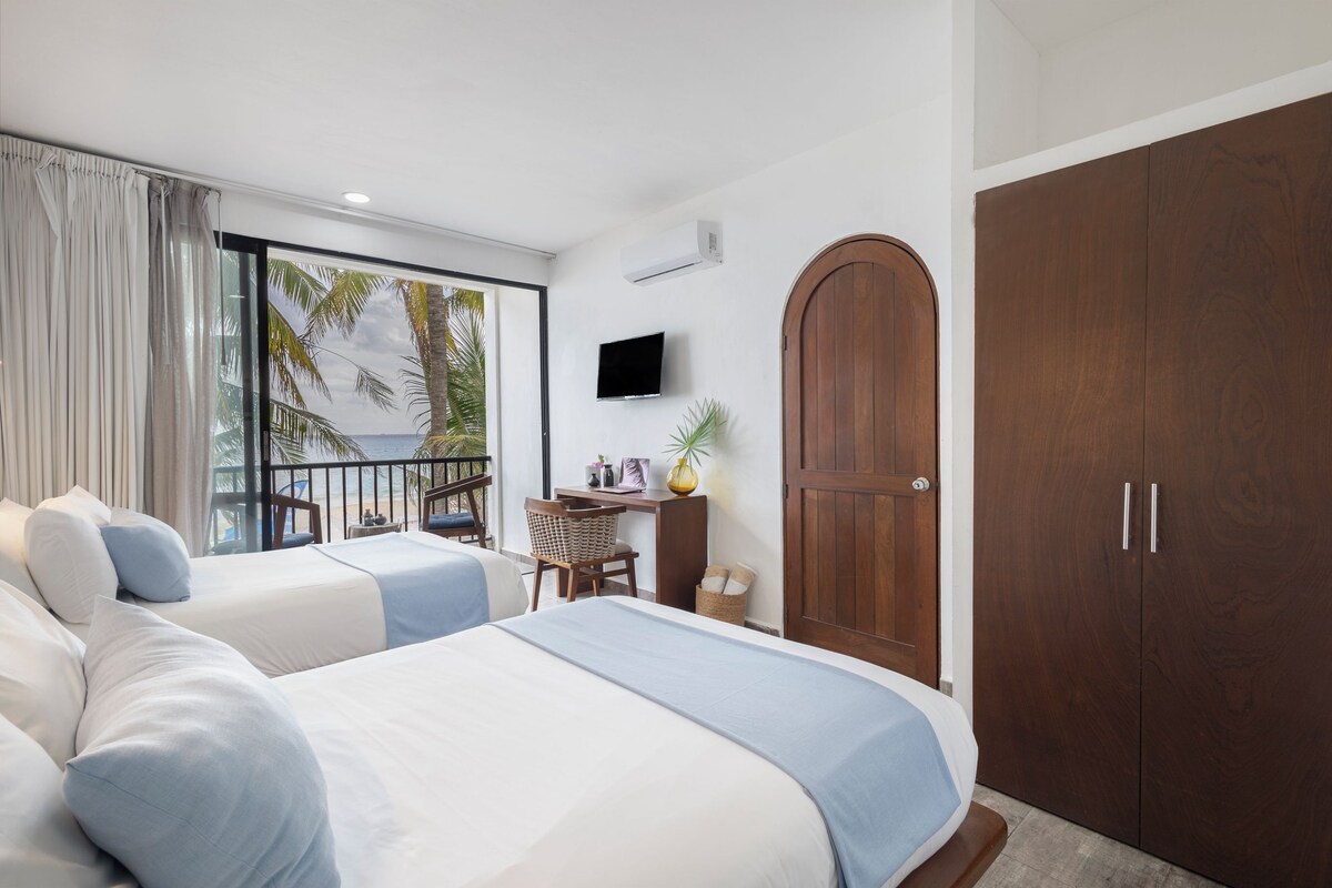 A hotel room with two beds, a desk, a TV, and a large wardrobe.