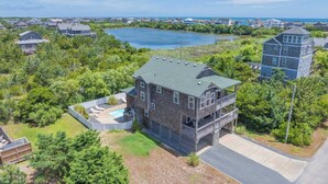 A two-story house with a balcony, surrounded by greenery and a lake. - Oceanside Home w/ Private Pool, Hot Tub, Game Rm. Snag this Message in a Bottle! (Salvo)
