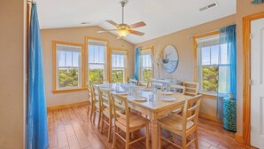 A dining area with a wooden table set for four, large windows with curtains, and a ceiling fan. - Oceanside Home w/ Private Pool, Hot Tub, Game Rm. Snag this Message in a Bottle! (Salvo)