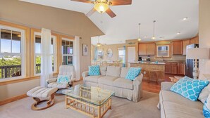 A spacious living room with a glass coffee table, a ceiling fan, and a view of the kitchen. - Oceanside Home w/ Private Pool, Hot Tub, Game Rm. Snag this Message in a Bottle! (Salvo)