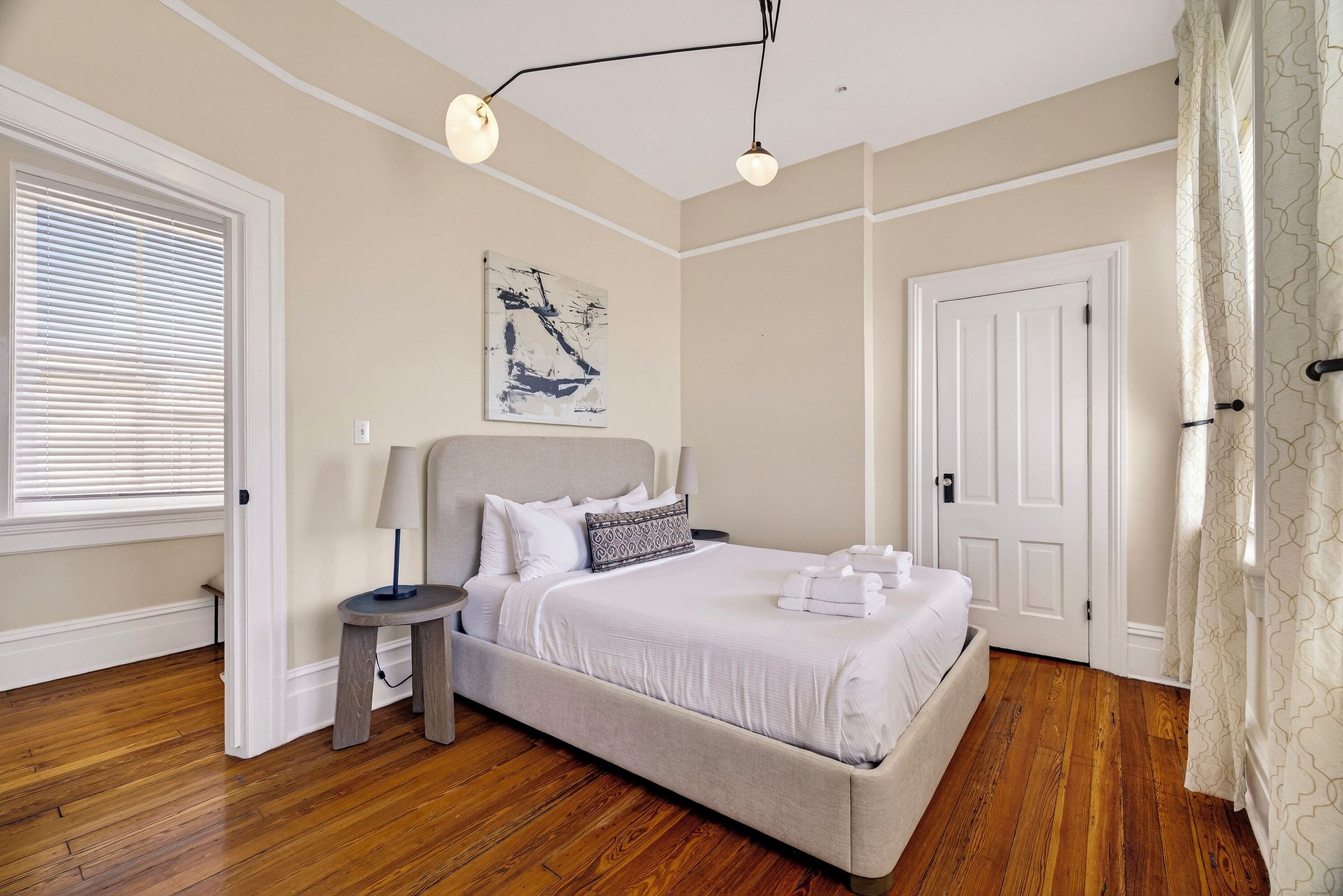A bedroom with a bed, bedside table, lamp, artwork, and a door.