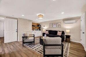 Un salon moderne avec un canapé noir, un fauteuil gris, une petite table basse et un tapis à motifs.