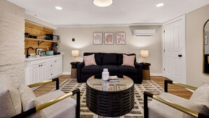A living room with a sofa, coffee table, and chairs, a kitchen area with cabinets and a microwave, and a ceiling light fixture.
