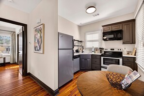 A modern kitchen with a refrigerator, stove, microwave, and a dining area with a table. - The Squares of Savannah: Light-filled Carriage House by Lucky Savannah (Savannah)