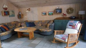 Un accogliente soggiorno con un divano in legno, una poltrona a dondolo e un tavolino da caffè. Presentano scaffali a muro e un piccolo mobiletto.