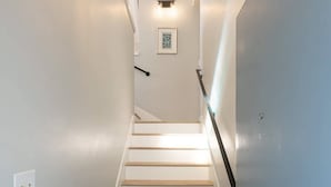 A staircase with wooden steps and white walls, leading to a landing with a light fixture and a framed picture. - 304 Ruby B | Balboa Island Charmer (Newport Beach)