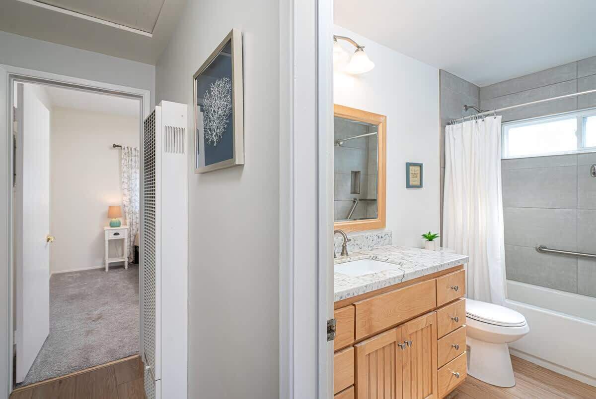 A modern bathroom with a marble sink, wooden cabinets, a glass shower enclosure, and a visible shower curtain.