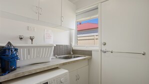 Ein kleiner Hauswirtschaftsraum mit einer Waschmaschine von Bosch, einem Waschbecken und einem Fenster mit Blick auf ein Gebäude mit rotem Dach.
