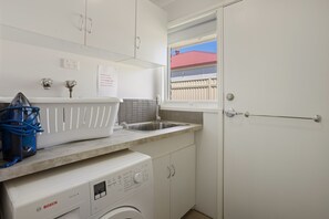 A compact laundry room with a Bosch washing machine, a sink, and a window with a view of a red-roofed building. - Rose by the Bay  Coastal Getaway in Tootgarook (Tootgarook)