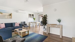 A modern living room with a sofa, coffee table, and a dining area with chairs and a table.