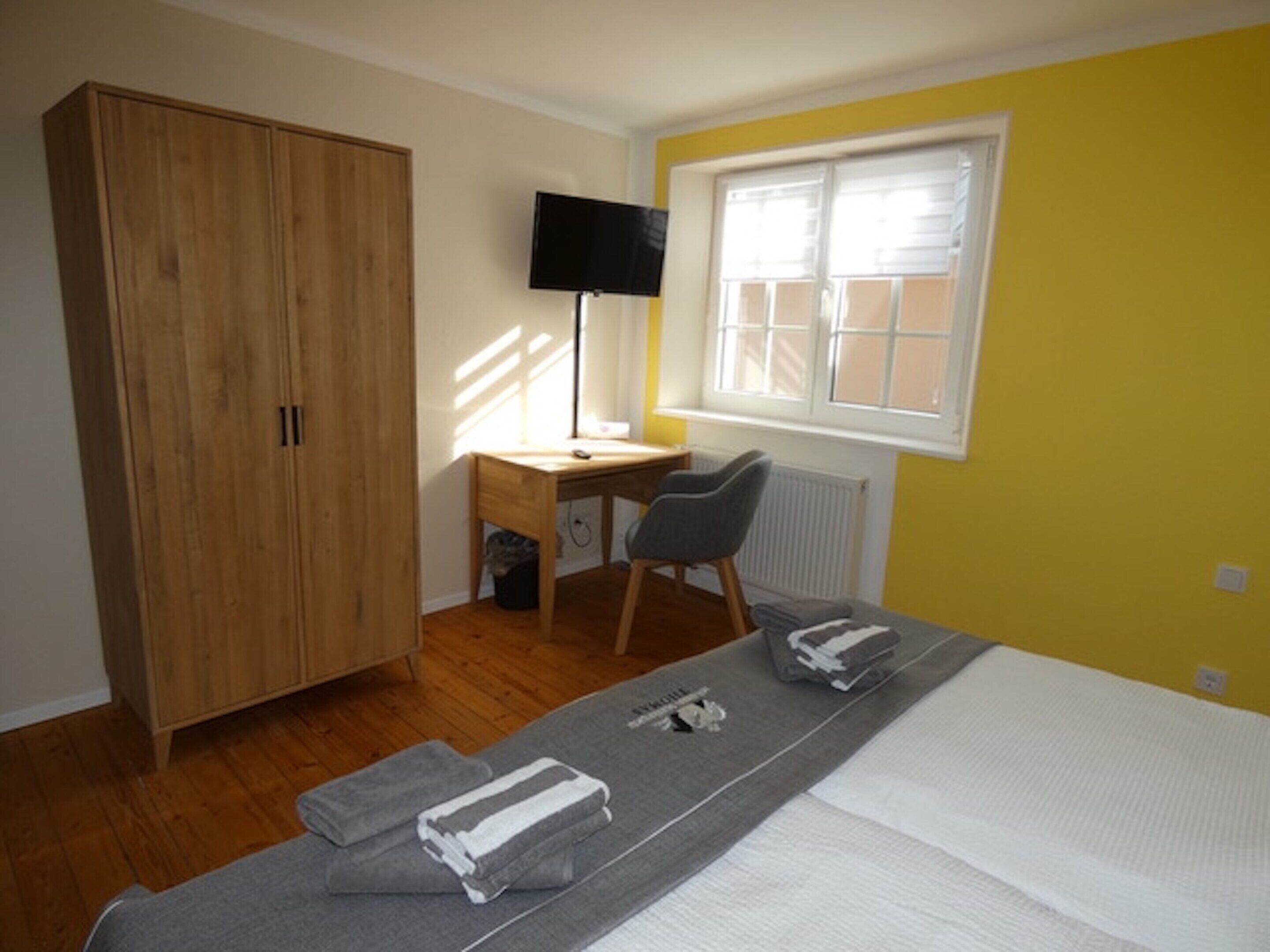 A bedroom with a bed, a desk, a chair, a wardrobe, and a TV.