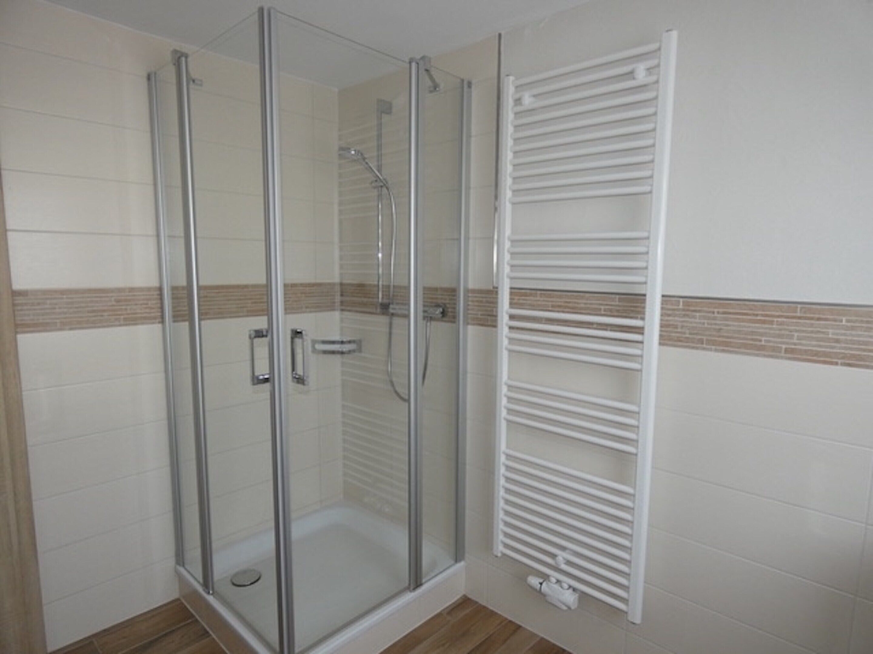 Une douche fermée par des parois de verre, avec un porte-serviettes blanc à côté.