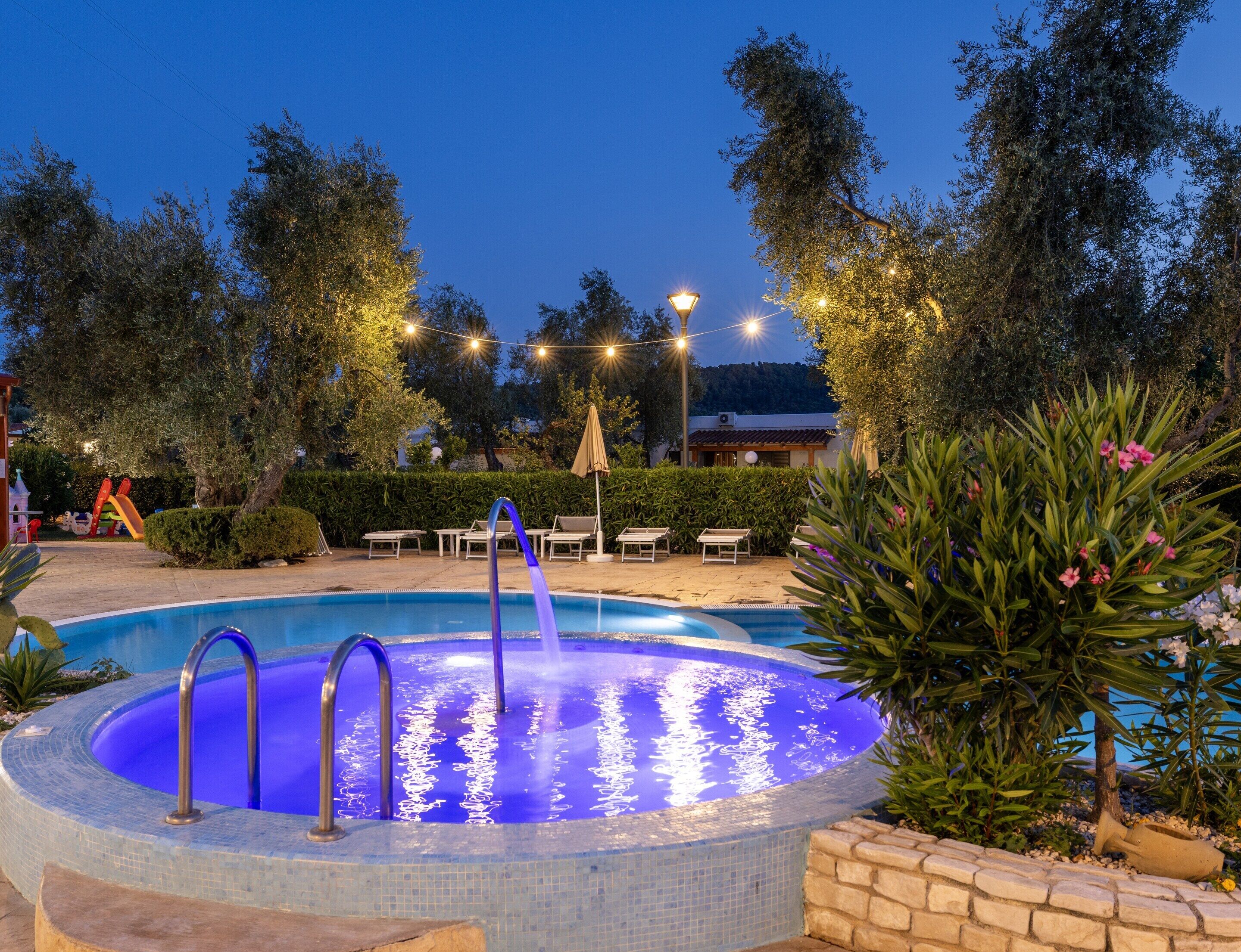 A swimming pool with a tiled edge, surrounded by greenery and outdoor furniture.