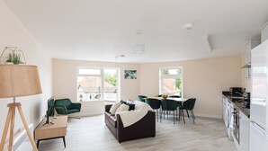 Een moderne woonkamer met een bank, stoelen, een eettafel en een keuken met apparatuur.