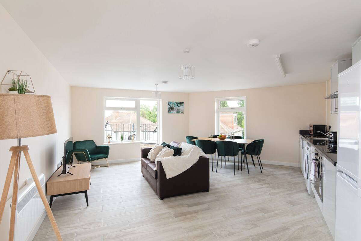 A modern living room with a sofa, chairs, a dining table, and a kitchen area with appliances.