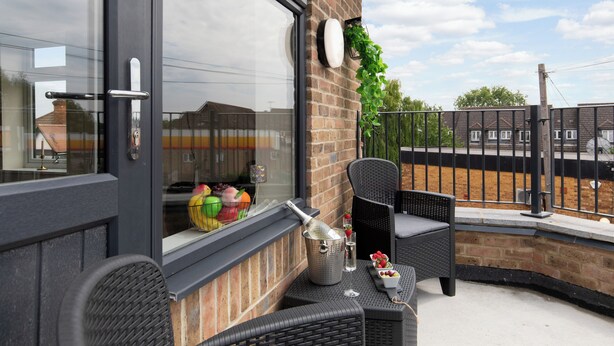 Een balkon met rieten meubilair, een barbecue en een schaal aardbeien.