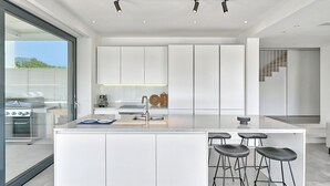 A modern kitchen with a large island, bar stools, and a view of the outdoors. - 5-bedroom Villa Near Split With Pool (Kastela)