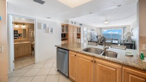 Een moderne keuken met granieten aanrechtbladen, roestvrijstalen apparatuur, houten keukenkastjes en uitzicht op de oceaan.