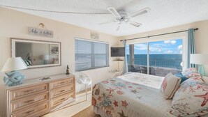 Een slaapkamer met een bed, een kaptafel, een spiegel, een plafondventilator en uitzicht op zee.