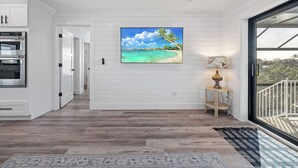 Una cocina moderna con hornos empotrados, piso de madera, un cuadro con temática de playa y vistas a través de una puerta de cristal.