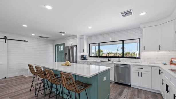 Una cocina moderna con una isla central, taburetes de bar y vistas al exterior.