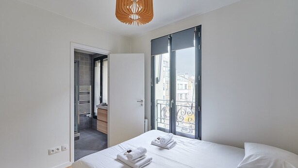 A modern bedroom with a large bed, a walk-in closet, and a balcony with a view of buildings.