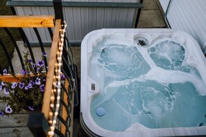 A hot tub with a control panel, surrounded by a wooden deck and potted plants. - Cypress-3BR|Hottub|PetFriendly (Olds)