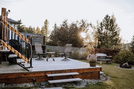 A wooden deck with outdoor seating, a grill, and a staircase leading to a covered area.. Cypress-3BR|Hottub|PetFriendly