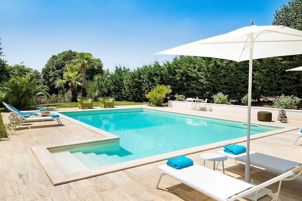 A swimming pool with lounge chairs and umbrellas, surrounded by greenery.