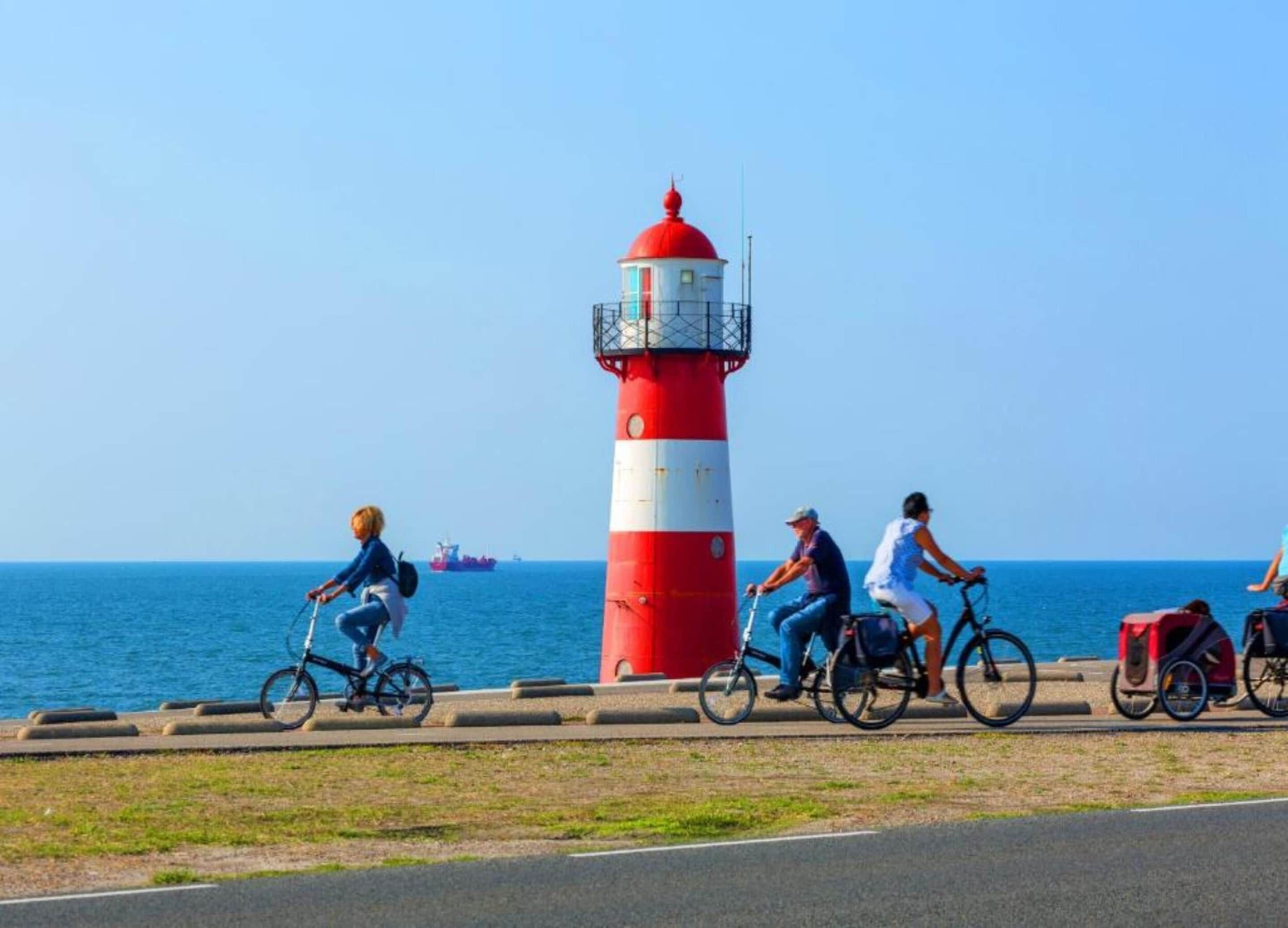 A red and white lighthouse with a clear view of the sea and a ship in the background.