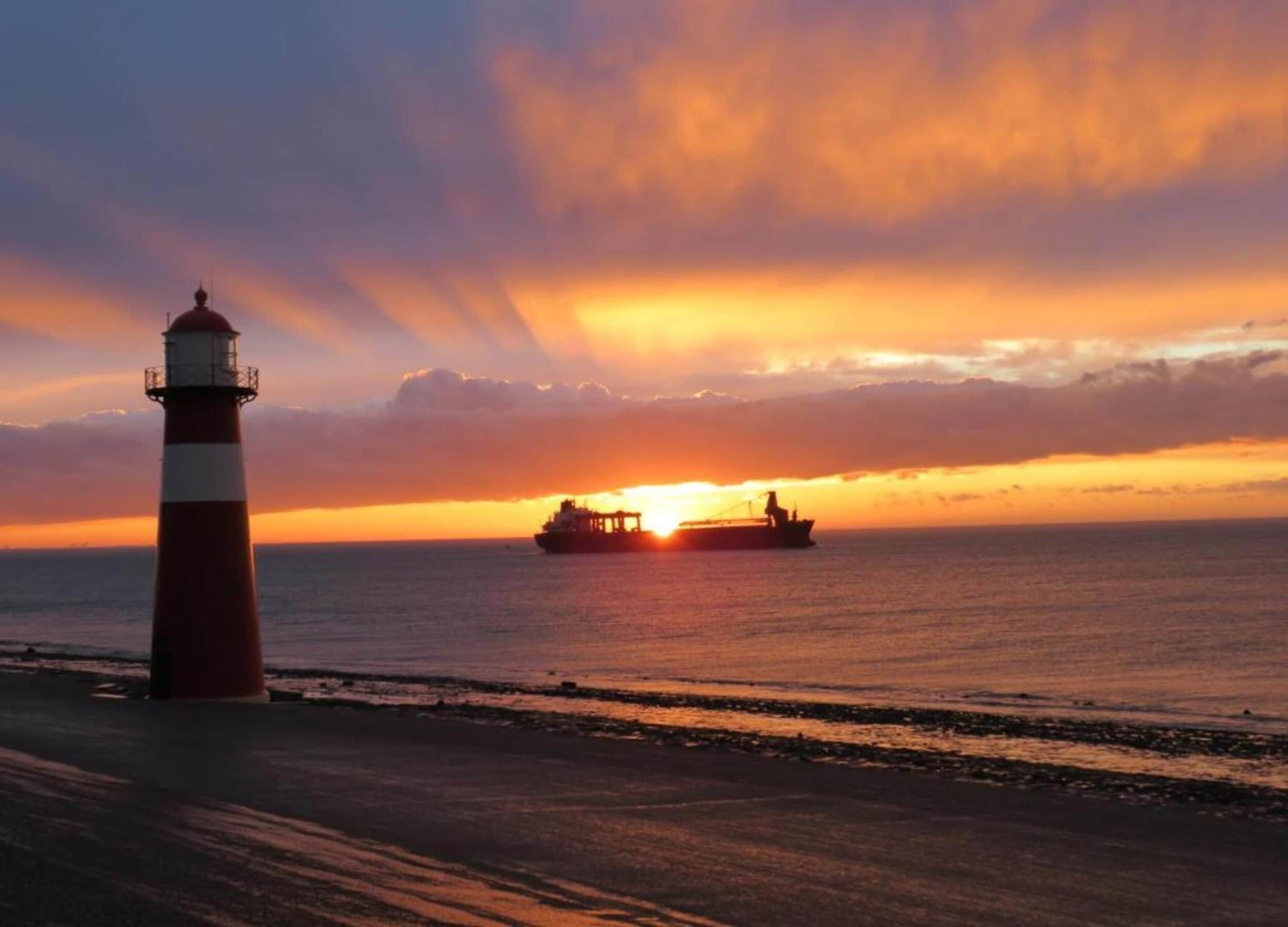 A lighthouse by the sea with a sunset in the background.