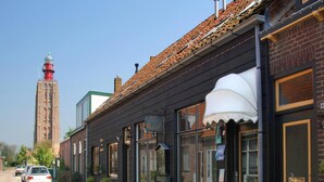 Una fila di edifici con ampie finestre e facciata in mattoni, una torre sullo sfondo e un'auto parcheggiata sulla strada.