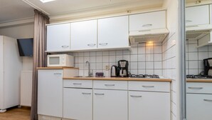 Una cucina compatta con mobili bianchi, un forno a microonde, una macchina da caffè e un fornello a gas.
