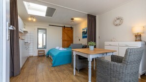 Una camera accogliente con un letto, un tavolo, sedie in vimini, una piccola panca, una pianta in vaso, una lampada e un armadio.