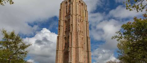 A tall brick tower with a red and white top, surrounded by trees and a partly cloudy sky.