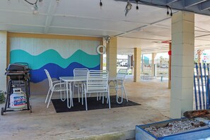 Relax in this outdoor seating area with a table, four chairs, and a grill, sheltered by a unique metal wall.