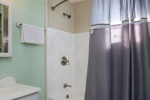 Bathroom features a white bathtub, sink, and shower area with a grid-patterned tile wall.