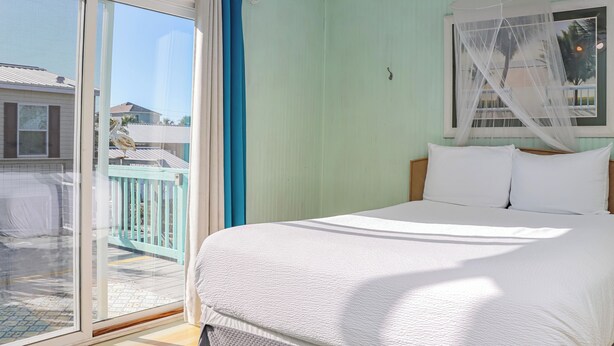 A bedroom with a large bed, a sliding glass door to a balcony, and a mosquito net over the window. - ☀️4BR-1 Block from Beach-Pet Friendly-Sea Hook☀️ (St. Joe Beach)
