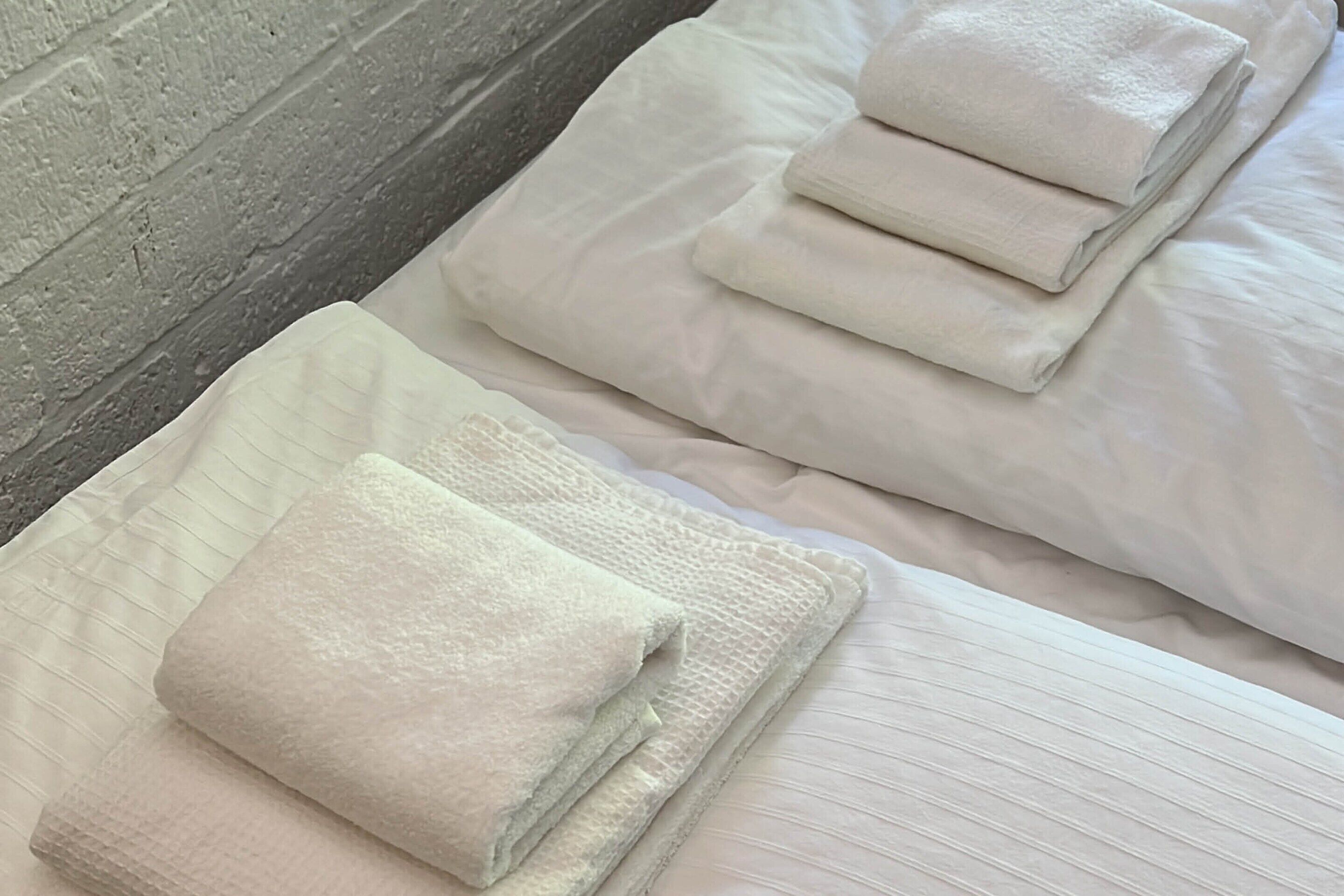 Ein ordentlich bezogenes Bett mit gefalteten weißen Handtüchern und einer gesteppten Decke.