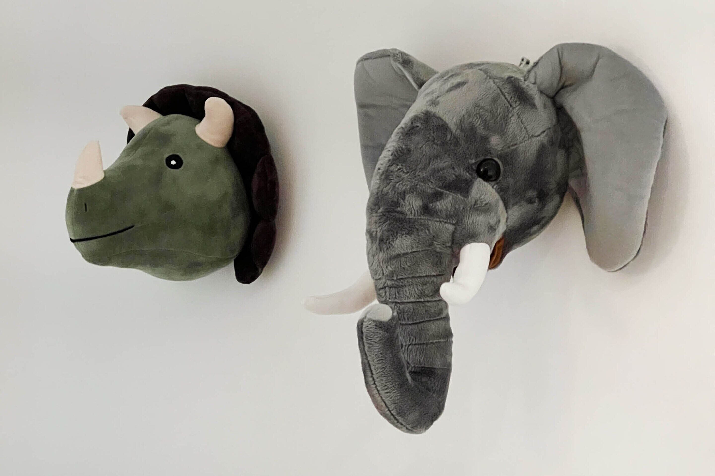 Dos esculturas de animales de peluche, una con forma de dinosaurio y la otra de elefante, fijadas a la pared.